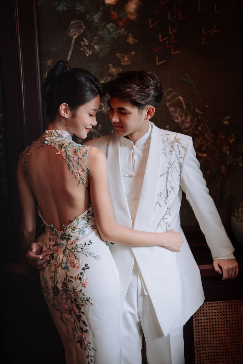 Elegant couple in traditional Chinese wedding attire featuring embroidered white qipao and matching suit.
