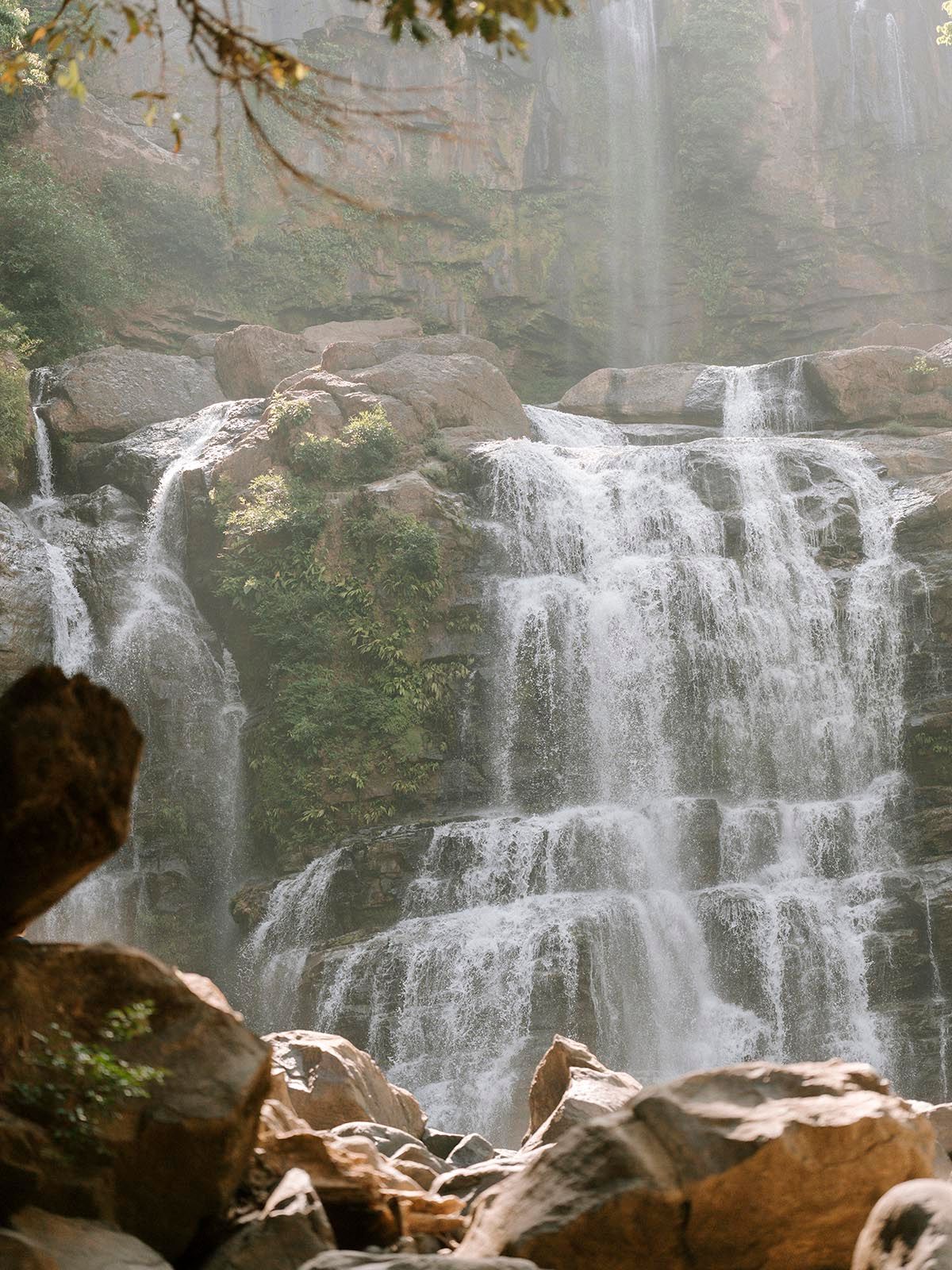 Majestic multi-tiered waterfall cascading over rocky cliffs in a misty forest setting. In Costa Rica