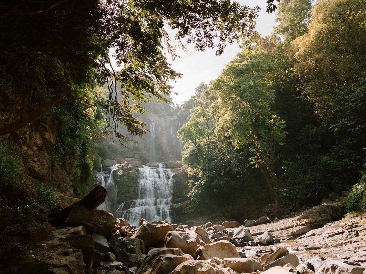 Scenic waterfall cascading down rocky cliffs surrounded by lush forest in natural light.