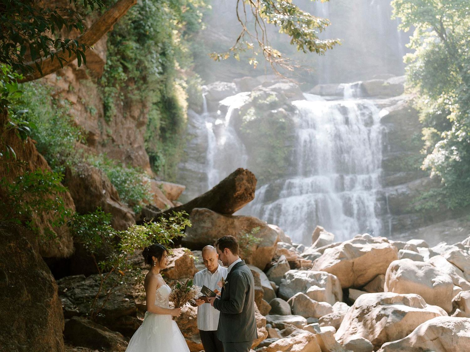 Intimate wedding ceremony set against backdrop of natural waterfall and rocks.