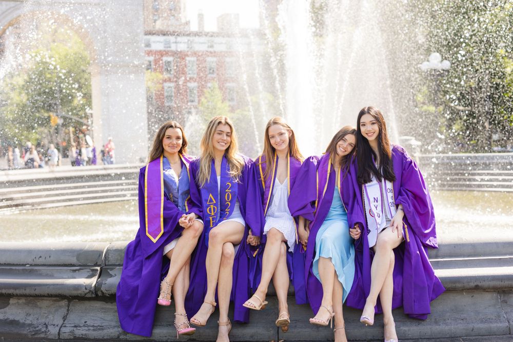 Group of graduates sitting on fountain ledge wearing purple graduation gowns.