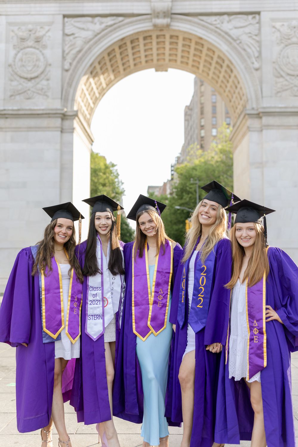 NYU graduates pose in purple robes under Washington Square Arch.