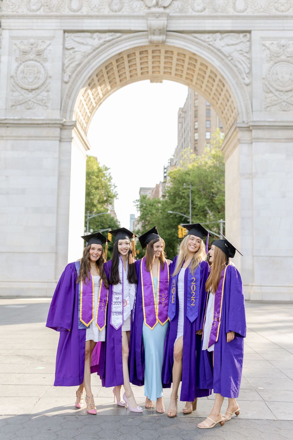 Graduation photo of purple-robed graduates posing together under a grand stone archway at NYU.