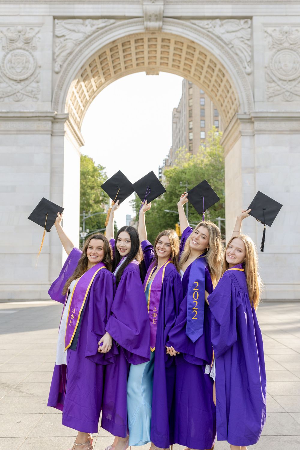 Graduates throwing graduation caps in celebration beneath a historic stone archway.