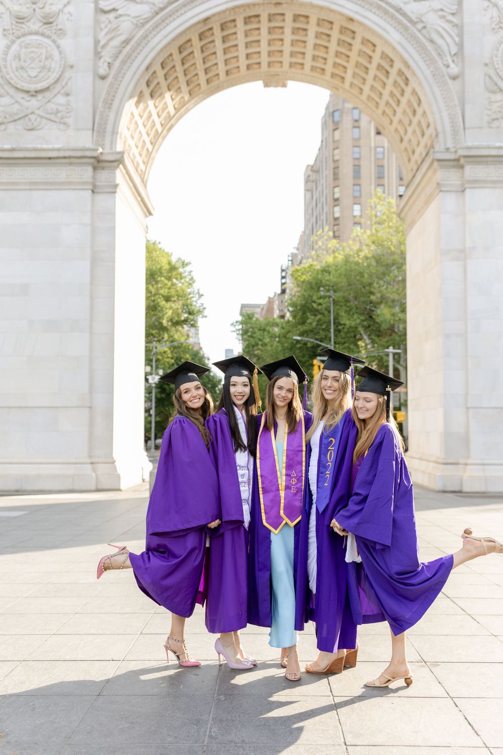 NYU graduates in purple regalia pose under the Washington Square Arch on graduation day.
