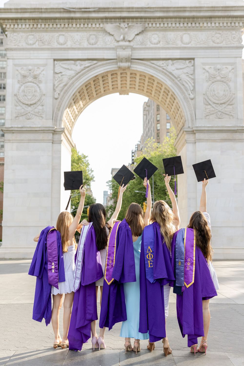 Graduates throw their caps in the air beneath a stone arch in celebration.