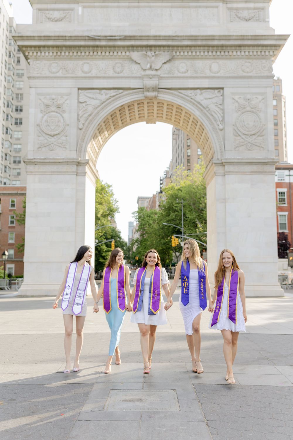 Graduates wearing purple stoles walk under the Washington Square Arch in NYC.