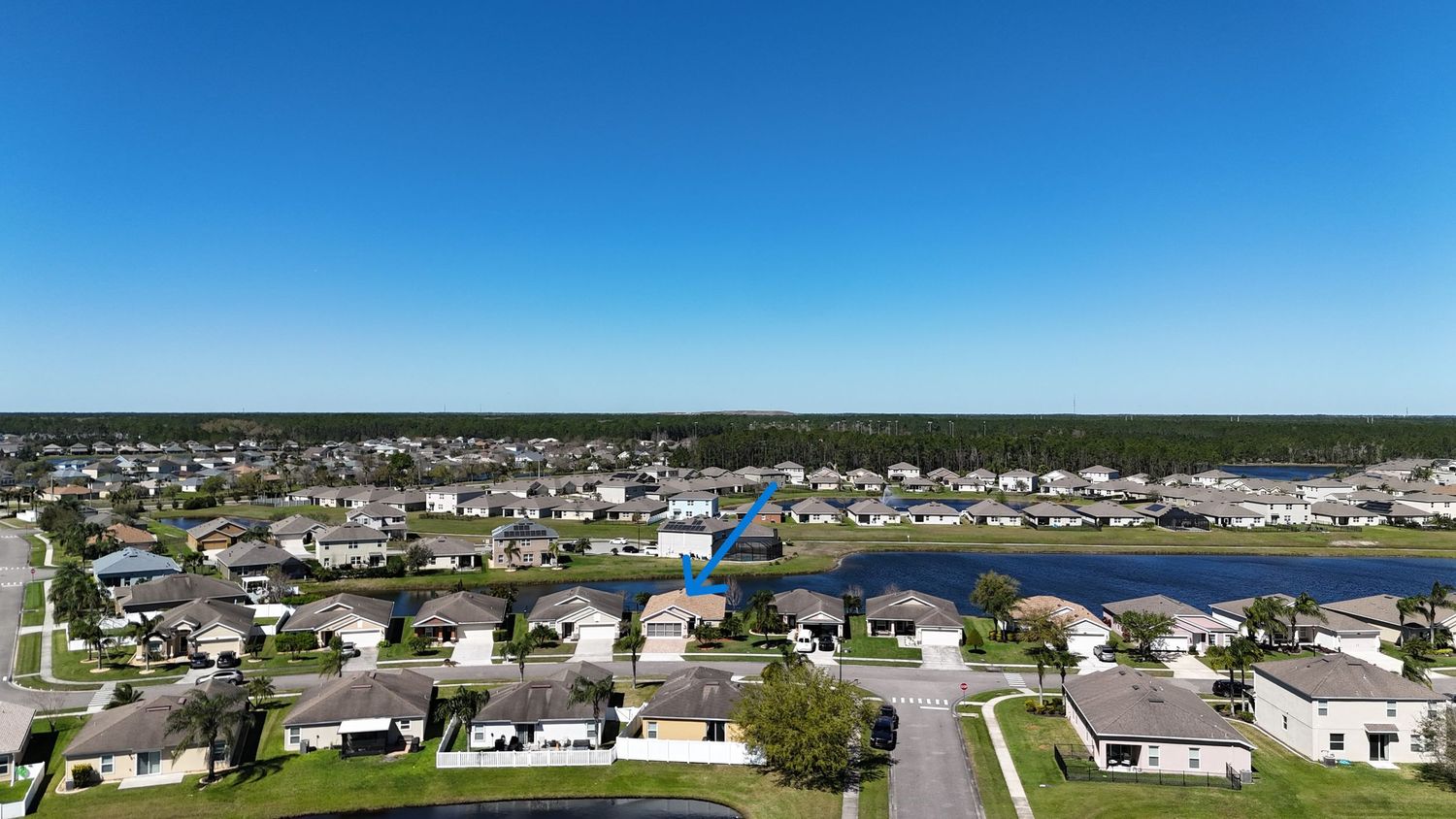 Panoramic aerial view of lakefront homes and community amenities under bright blue skies.