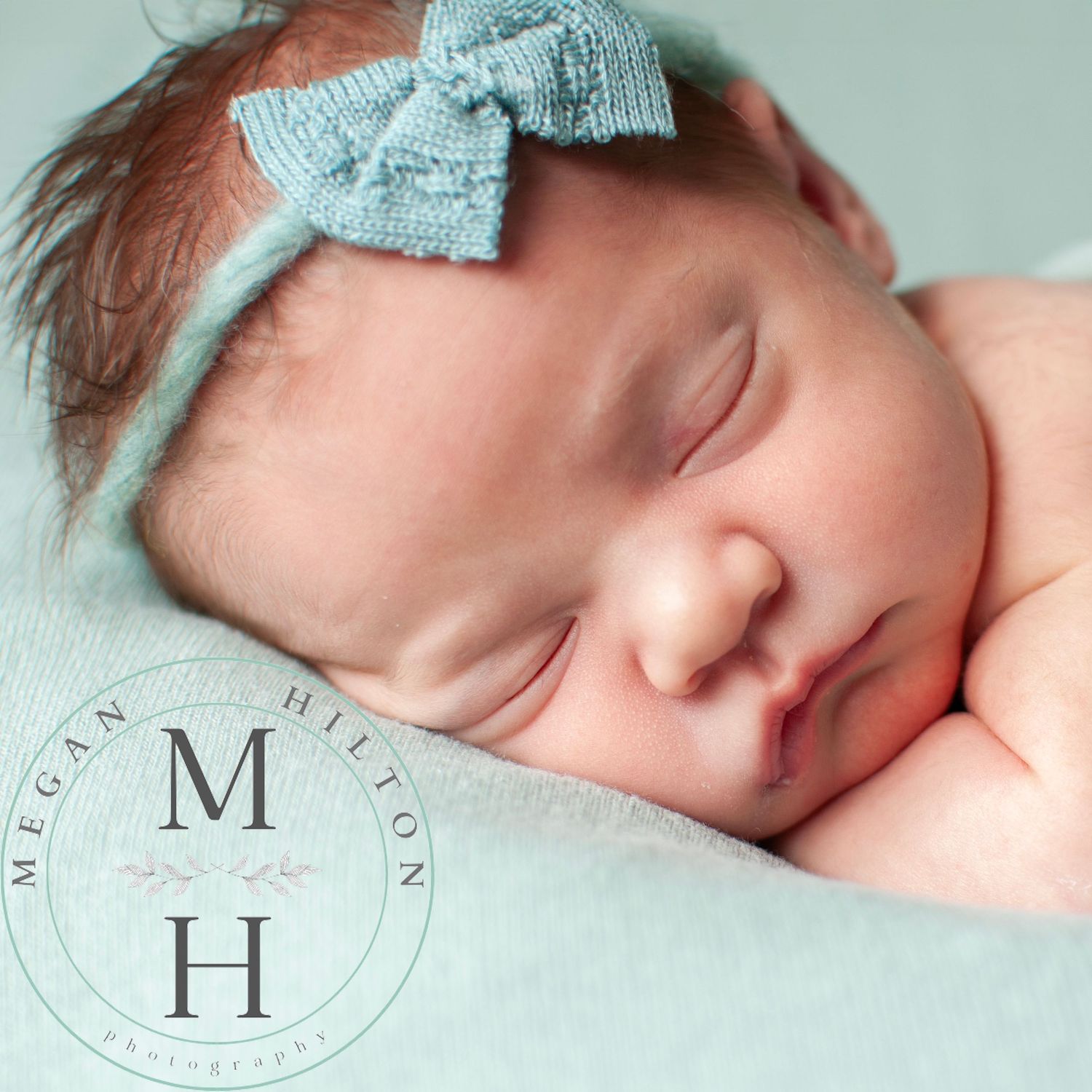 Sleeping newborn wearing a light green bow headband resting peacefully on mint backdrop photo.