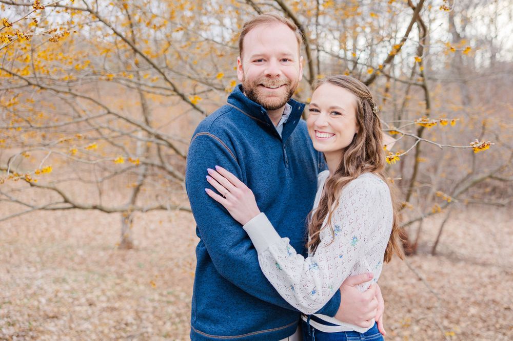 A smiling couple poses for their engagement photos in a fall setting.