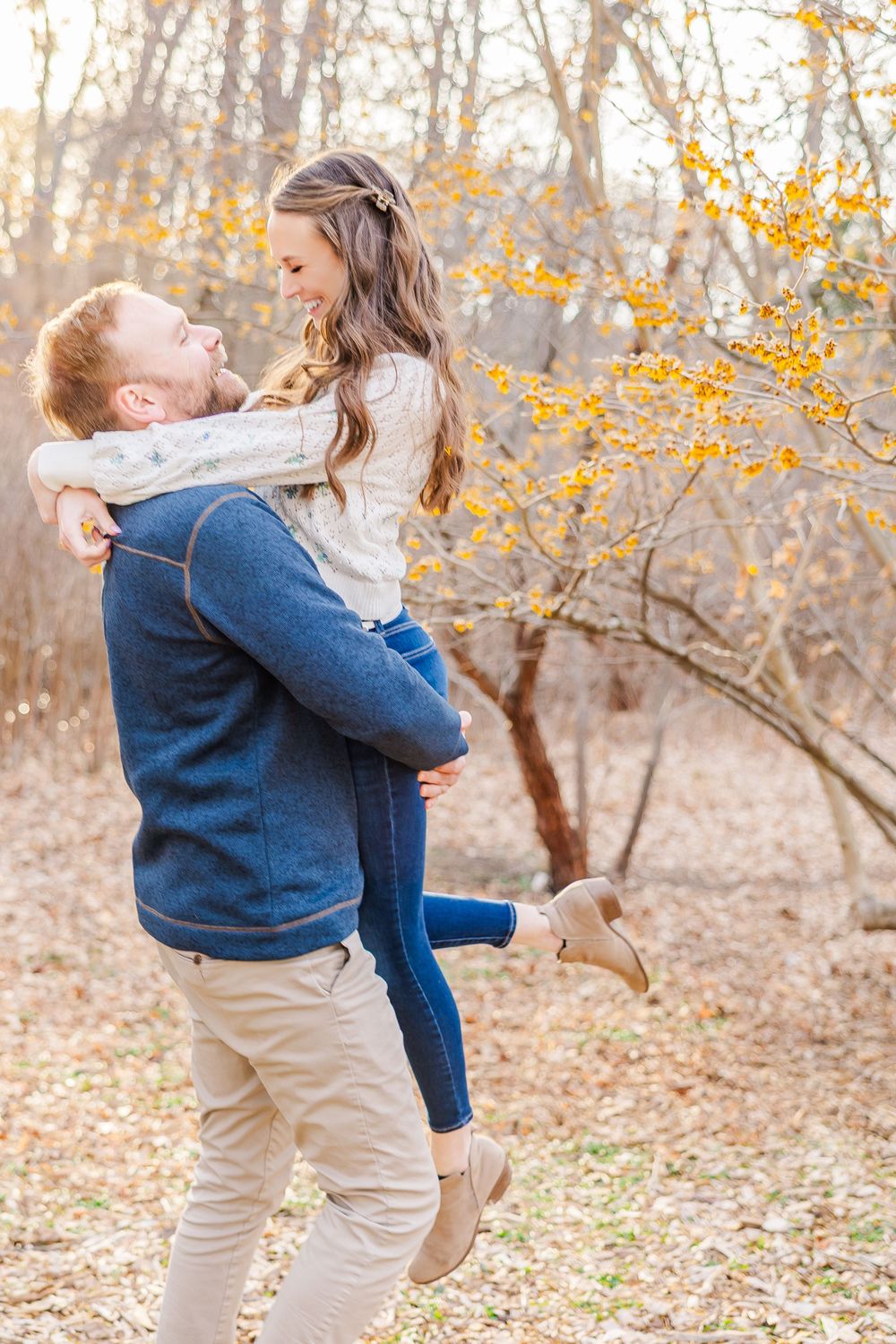 Playful couple shares a joyful moment as he lifts her up against a backdrop of golden autumn leaves.