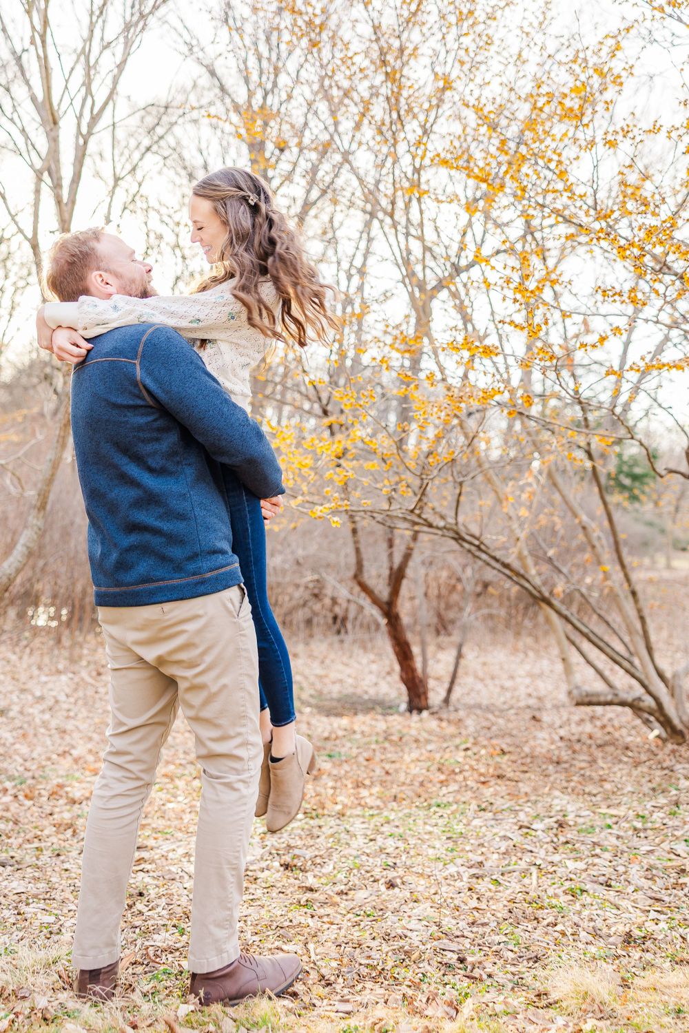 Romantic lift pose during an autumn engagement photoshoot with yellow leaves in the background.