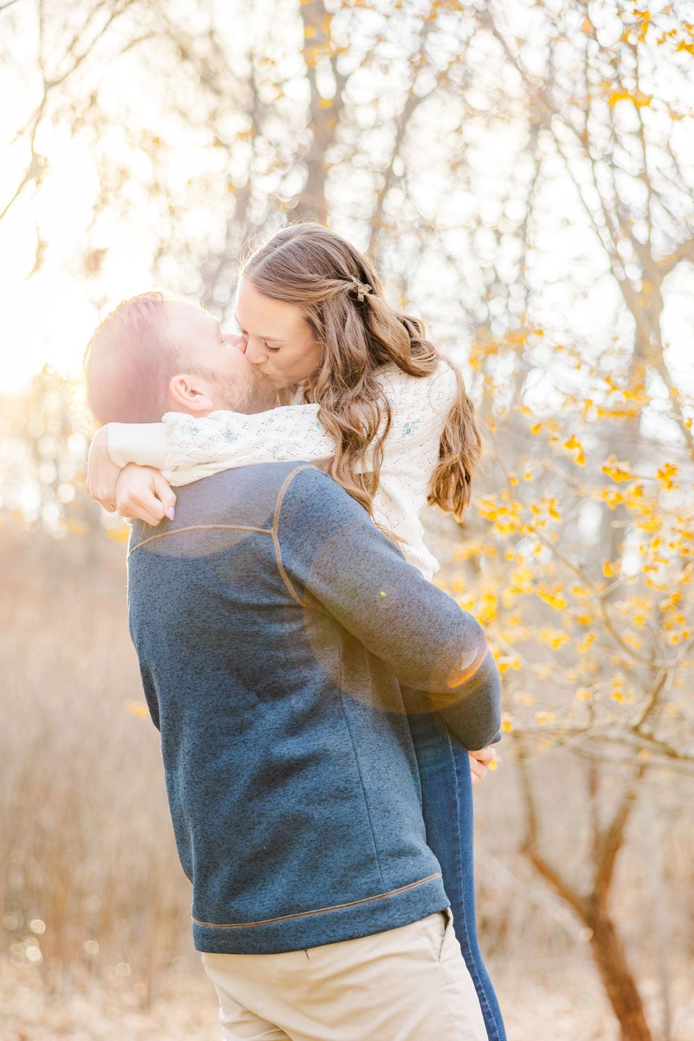 Couple sharing a tender moment during sunset engagement photos with golden fall foliage.