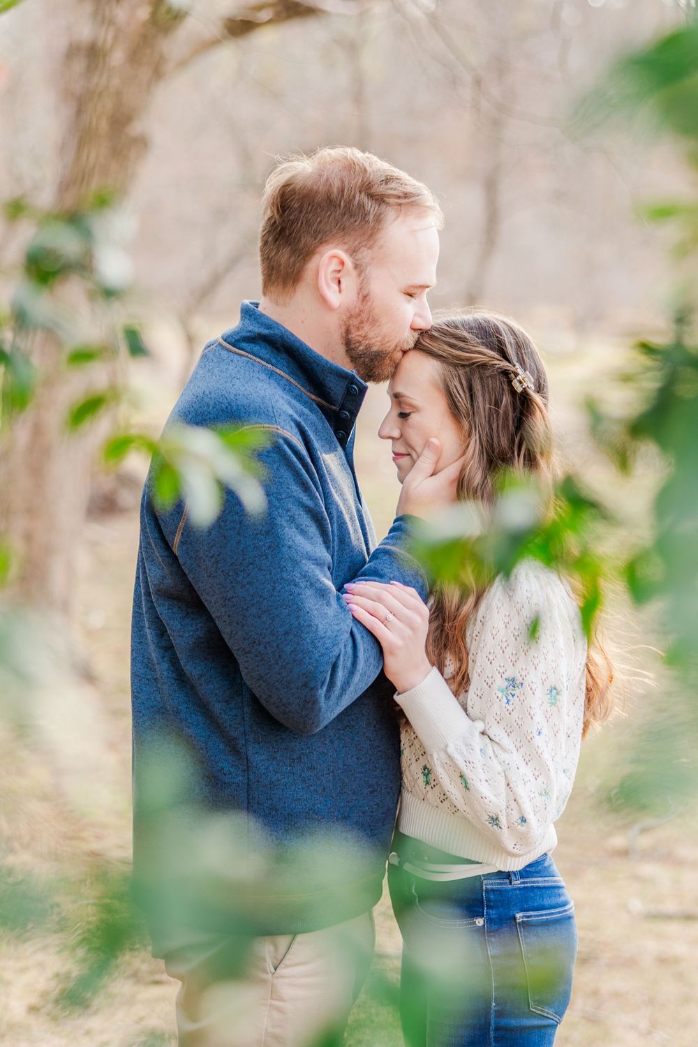 Intimate embrace captured through green leaves during outdoor engagement photography session.