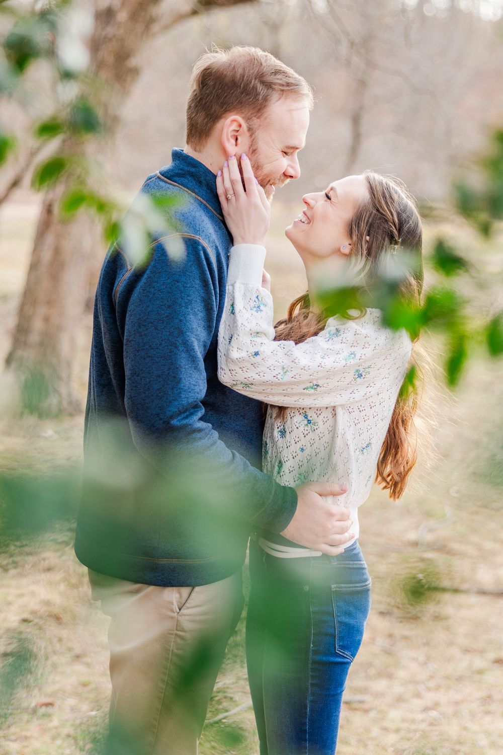 Tender moment between couple framed by soft green foliage during engagement photoshoot.