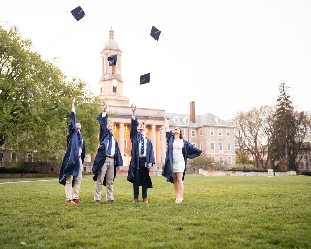 Graduation celebration on a college campus lawn with caps being thrown in the air near historic chapel building.