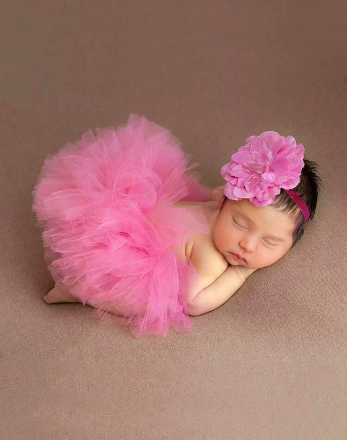 Sleeping newborn wearing pink tutu and headband in professional portrait.