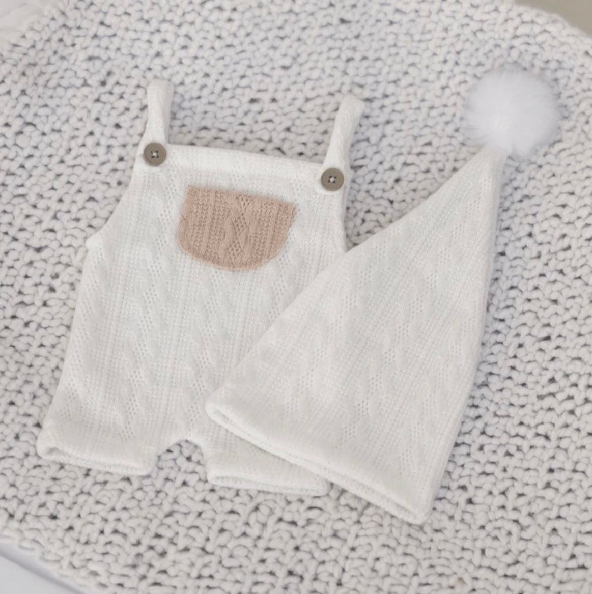 White knitted baby romper with contrast pocket displayed on lace background.