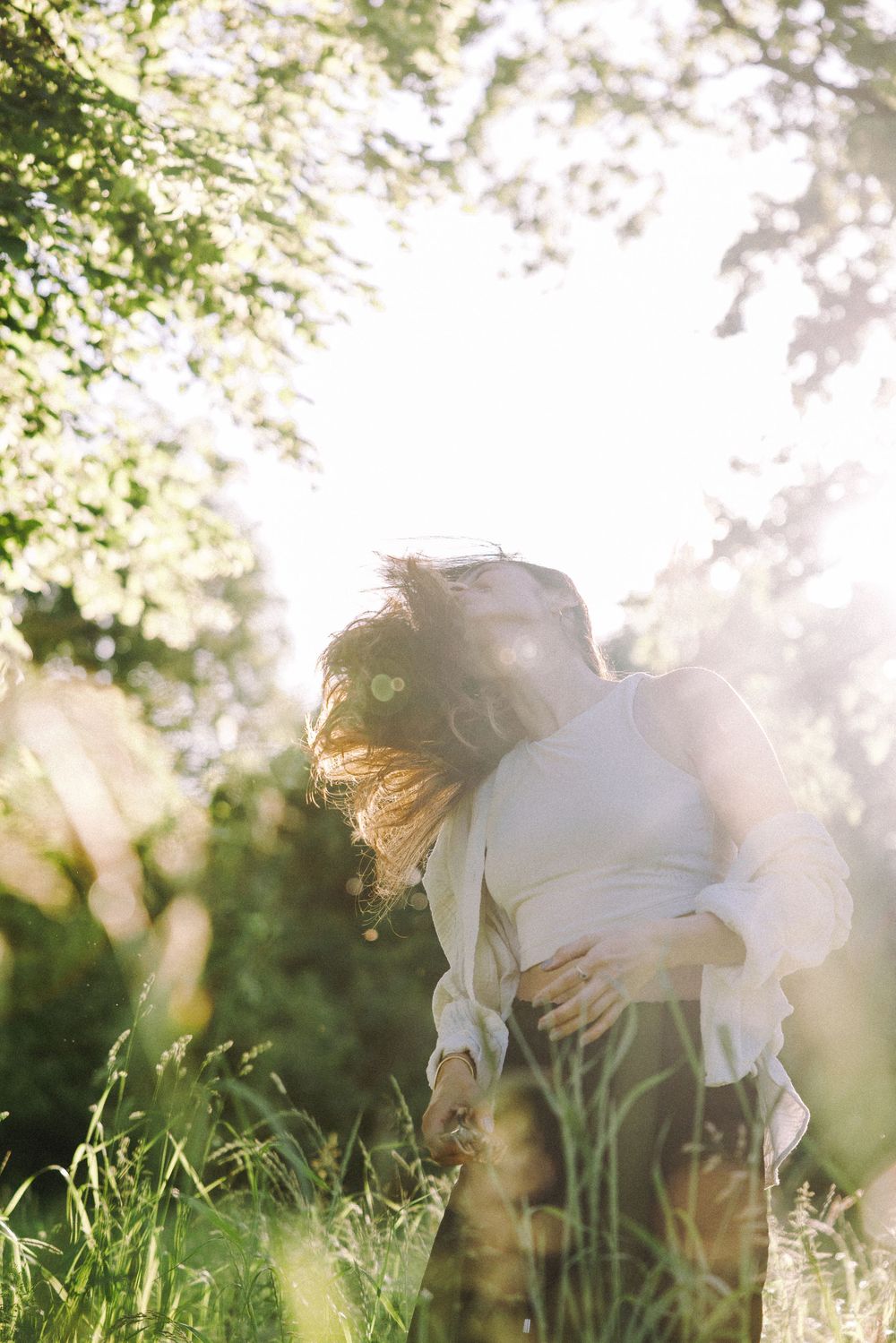 Ethereal backlit scene of someone in white clothing among grass and trees.