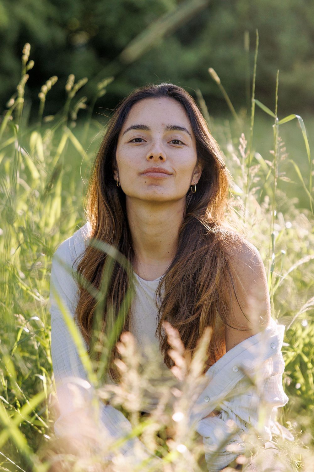 Person in white sweater sitting among tall grass in warm summer sunlight.