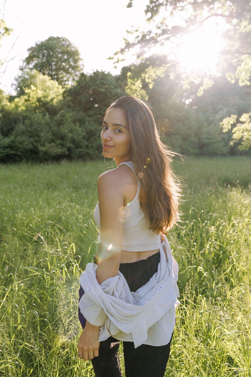 Woman in white top and black pants posing playfully in a golden meadow at sunset.