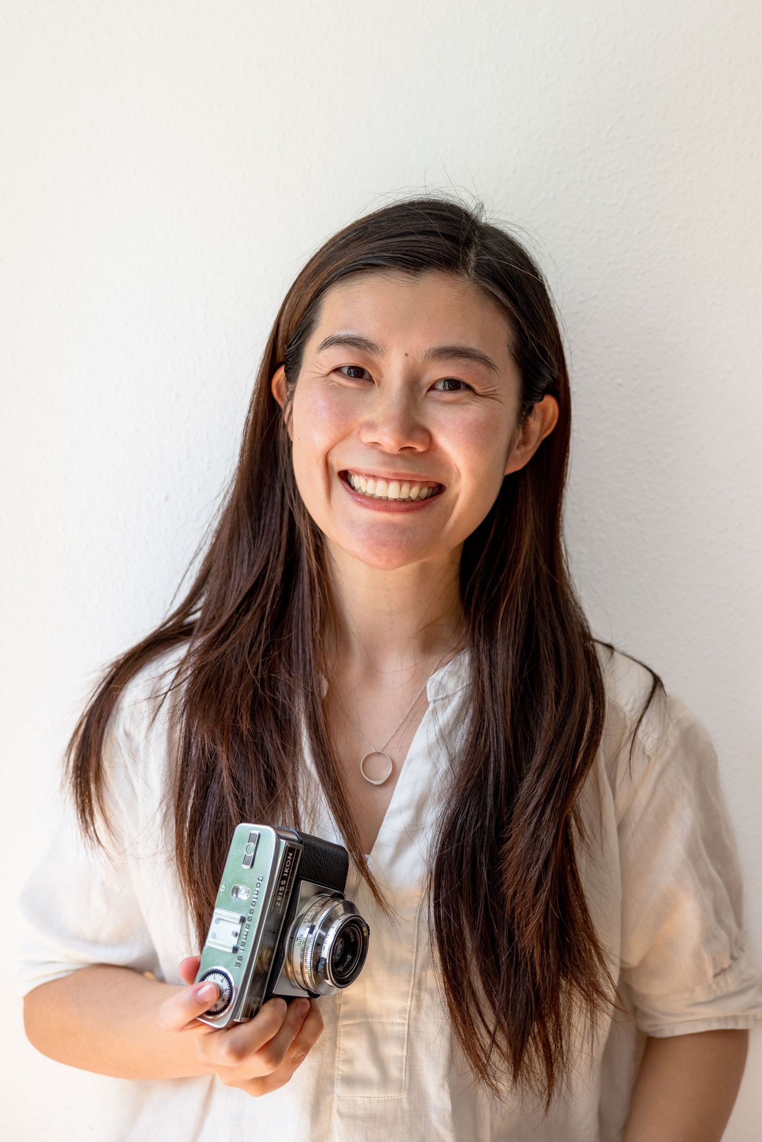 Person in white shirt poses playfully with vintage camera against white background.