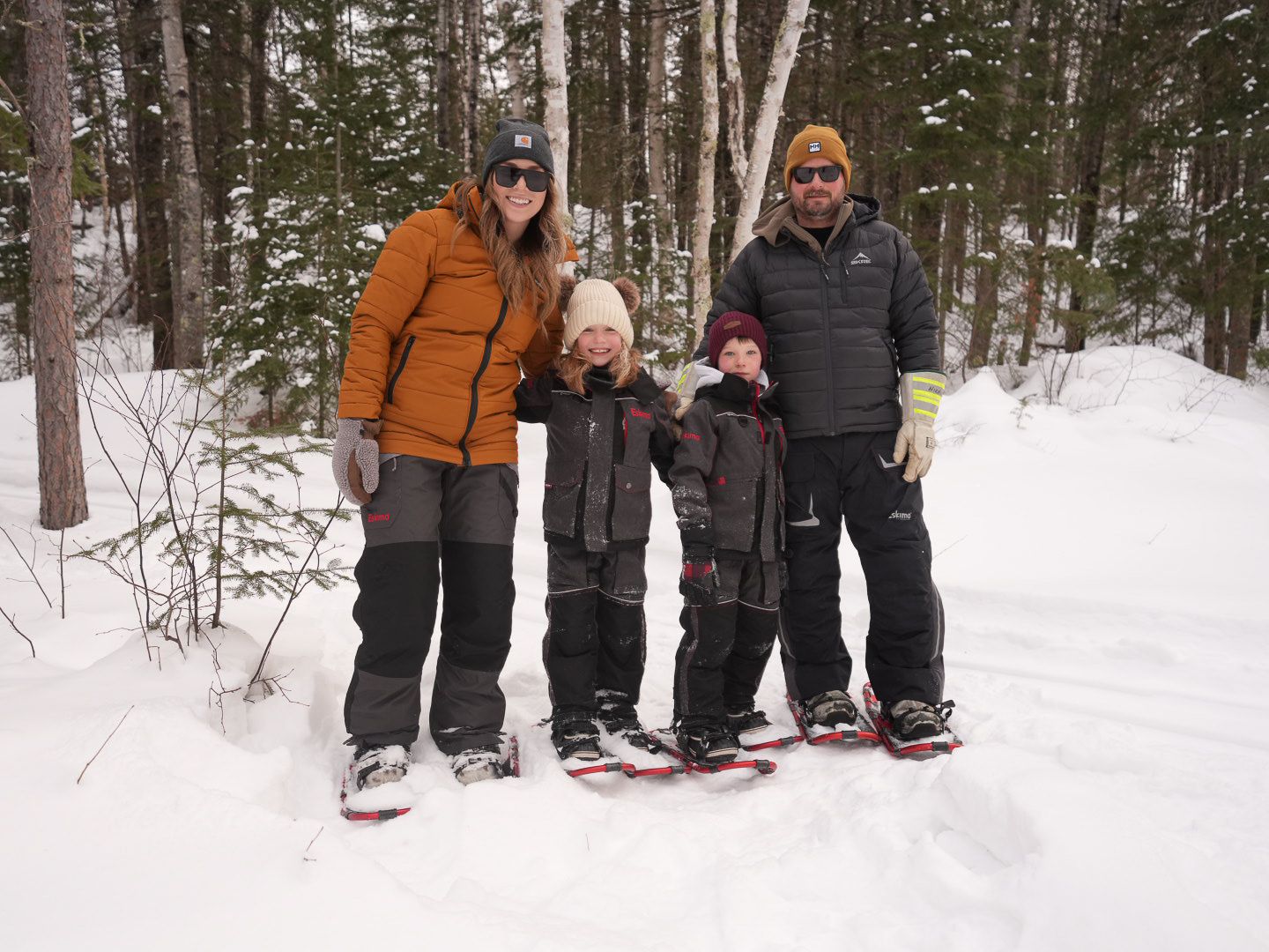 Group snowshoeing through a snowy winter forest trail surrounded by tall evergreen trees.