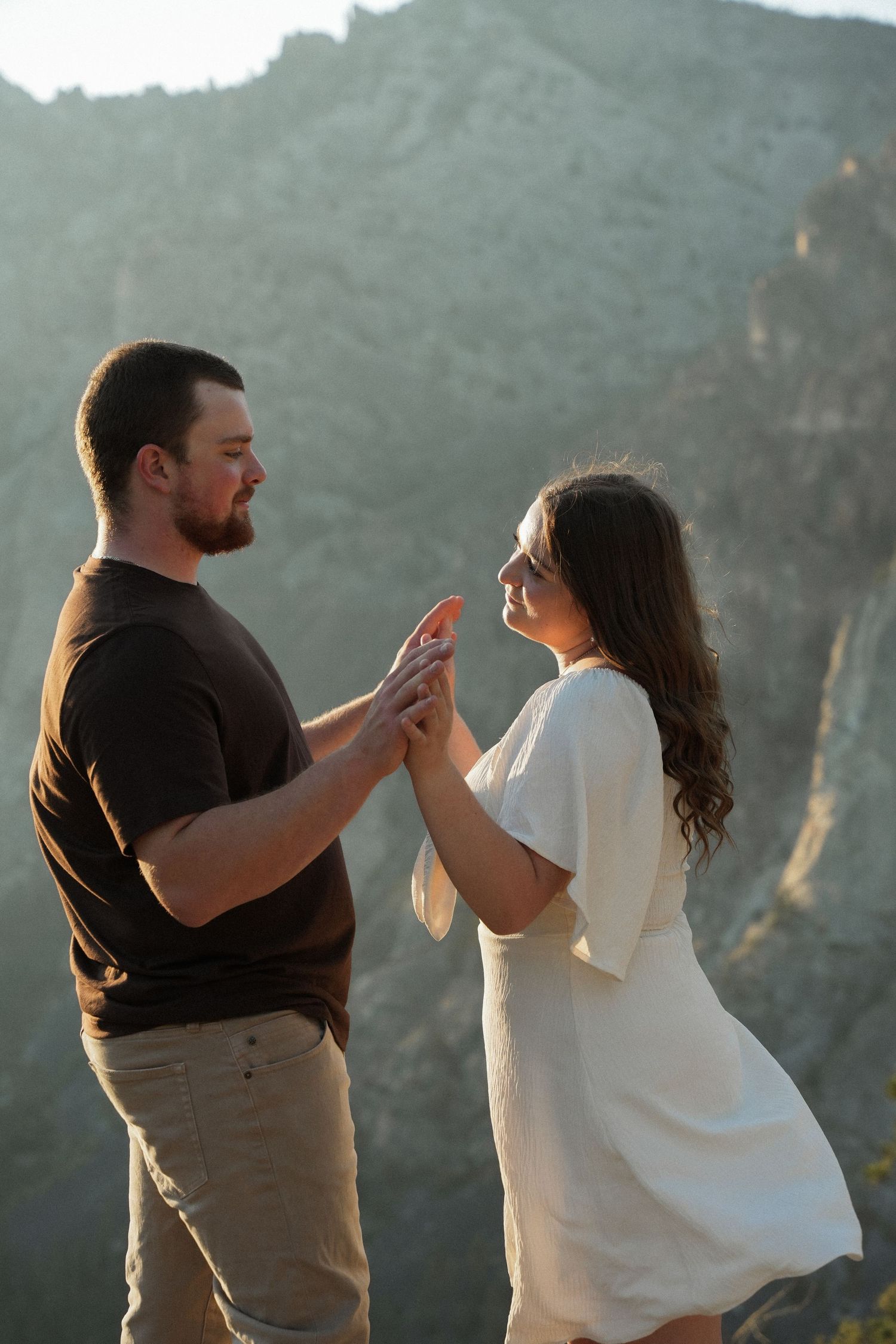 A couple dances together against a scenic mountain backdrop at sunset in a romantic outdoor setting.