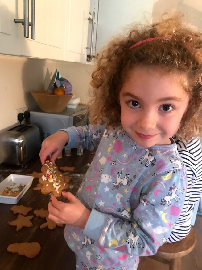 A child wearing a unicorn print shirt decorates holiday cookies at a kitchen counter.