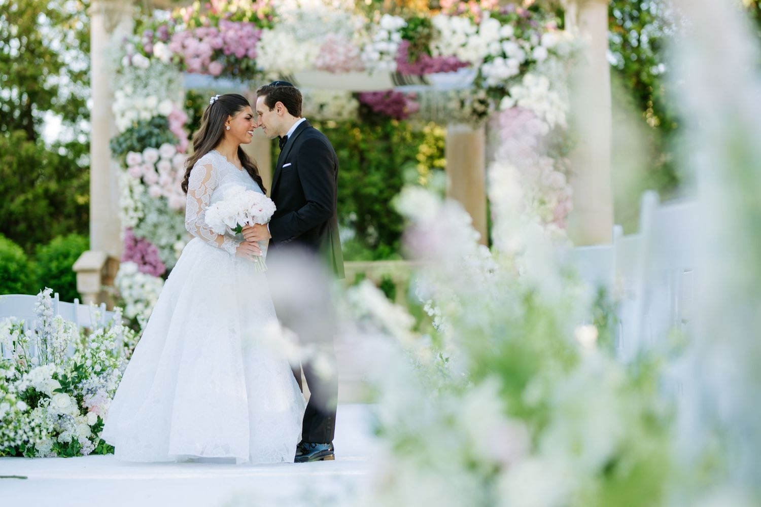 Intimate garden wedding ceremony surrounded by white and purple floral arrangements.
