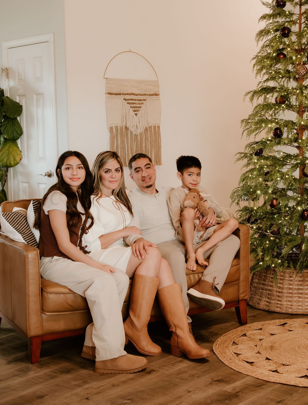 A group sits together on a brown leather couch with indoor plants and a woven basket visible in the background.
