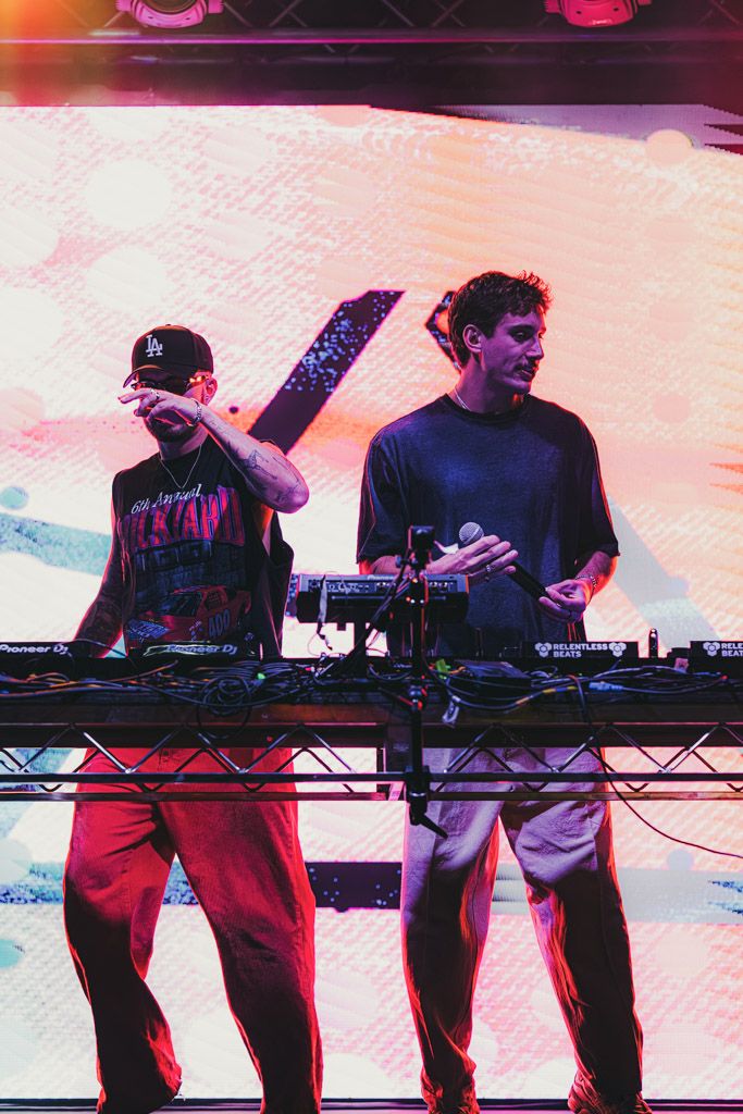 Multiple DJs working turntables and mixers on stage with pink and orange lighting effects.