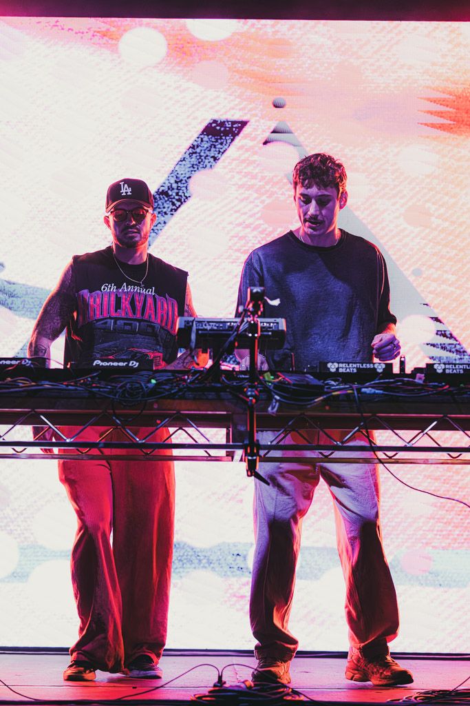 DJs performing with mixers and controllers on stage with pink ambient lighting.