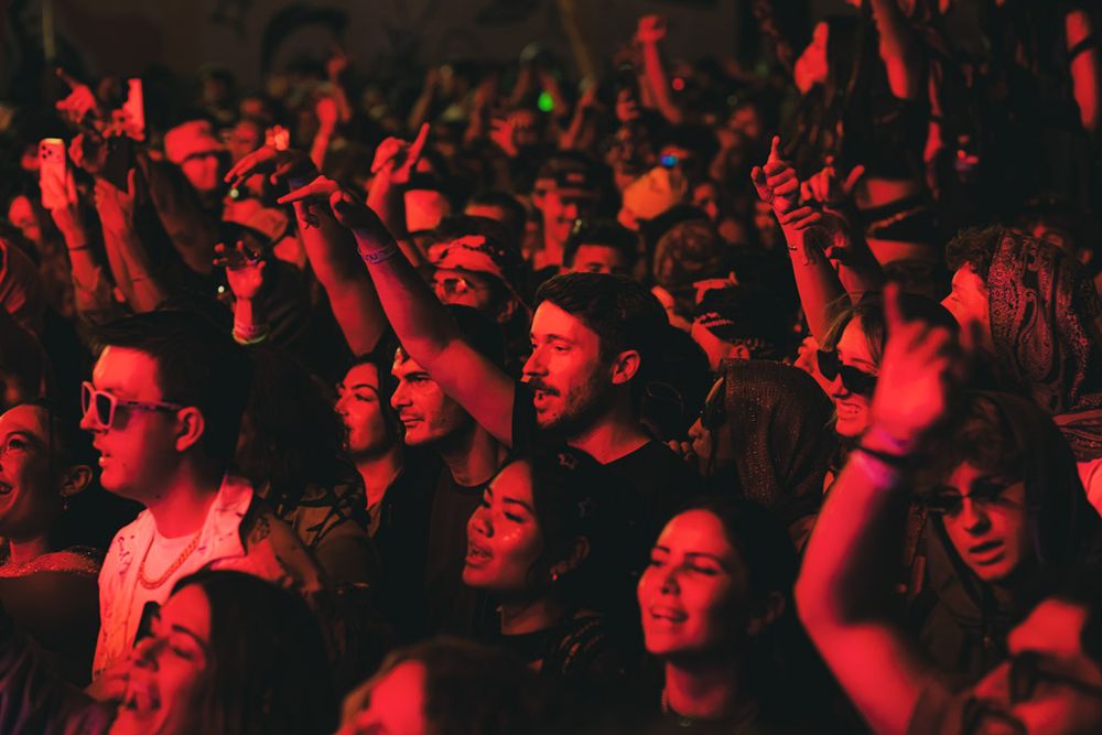 Concert crowd illuminated in red lighting cheers enthusiastically during live music performance.