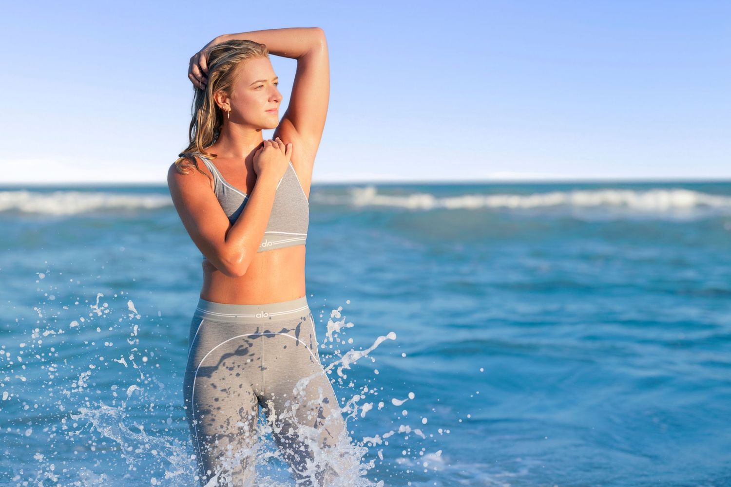 Athletic woman splashing in blue ocean waves wearing workout attire on a sunny day.