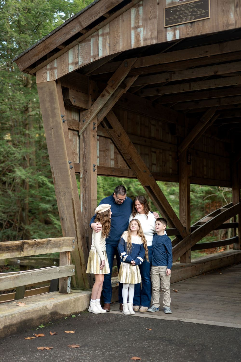 Family of five sharing a warm moment under the wooden beams of a rustic covered bridge.
