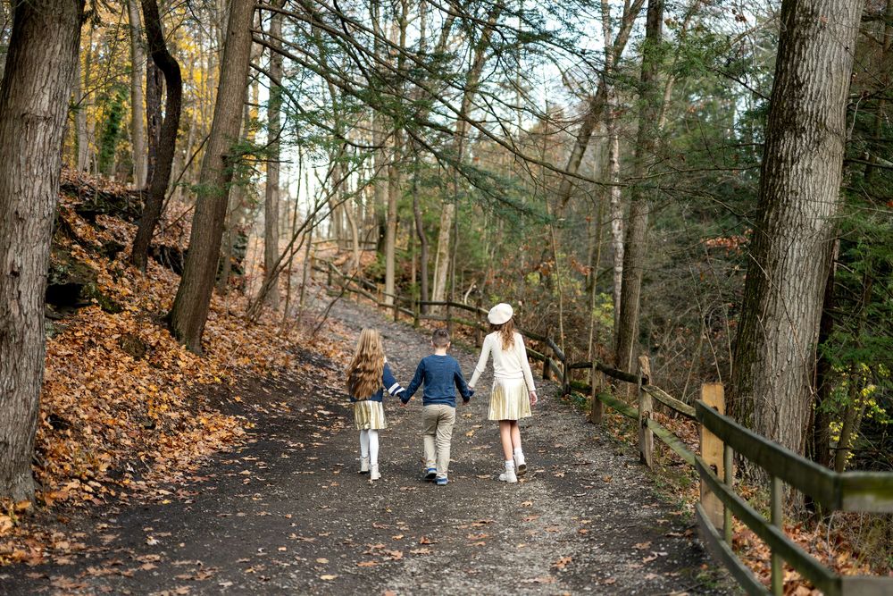 Woman and two children walking hand in hand along a scenic autumn forest path.