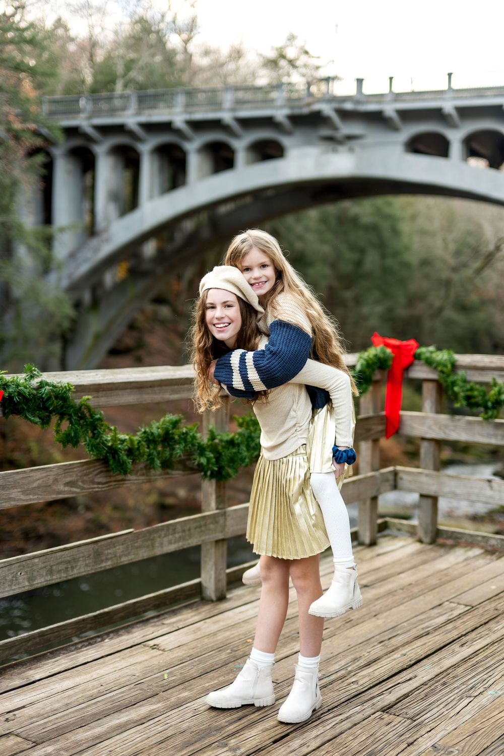 Teenage girl giving younger girl a piggyback ride on festive holiday decorated bridge.