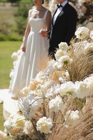 The couple holding hands during the ceremony with sculptural florals in the background.