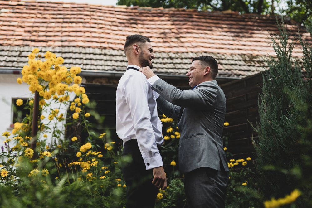 Groomsmen adjust ties and prepare formal attire in outdoor garden setting.