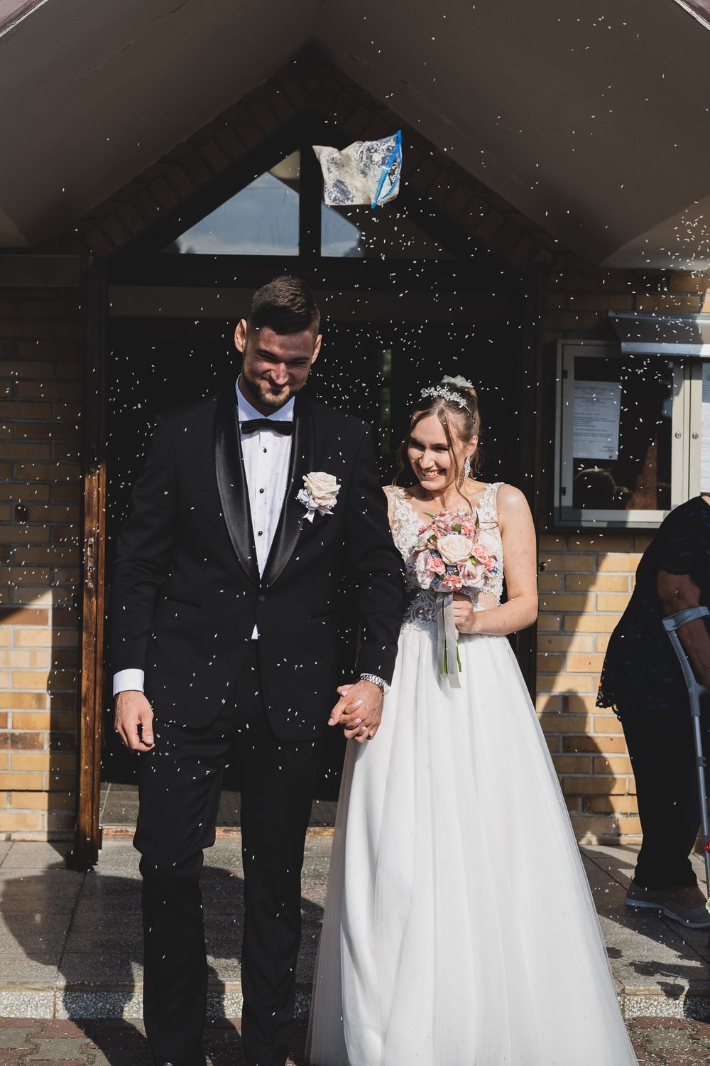 Wedding party exits church ceremony while guests throw confetti in celebration.