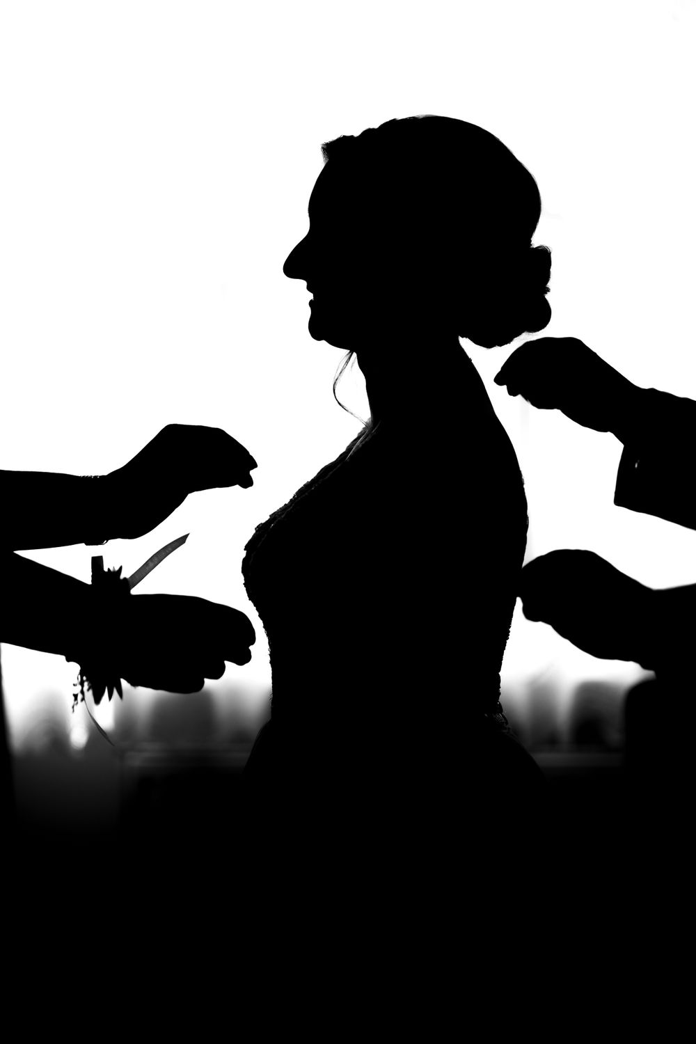 A dramatic silhouette shows hands helping with wedding preparations.