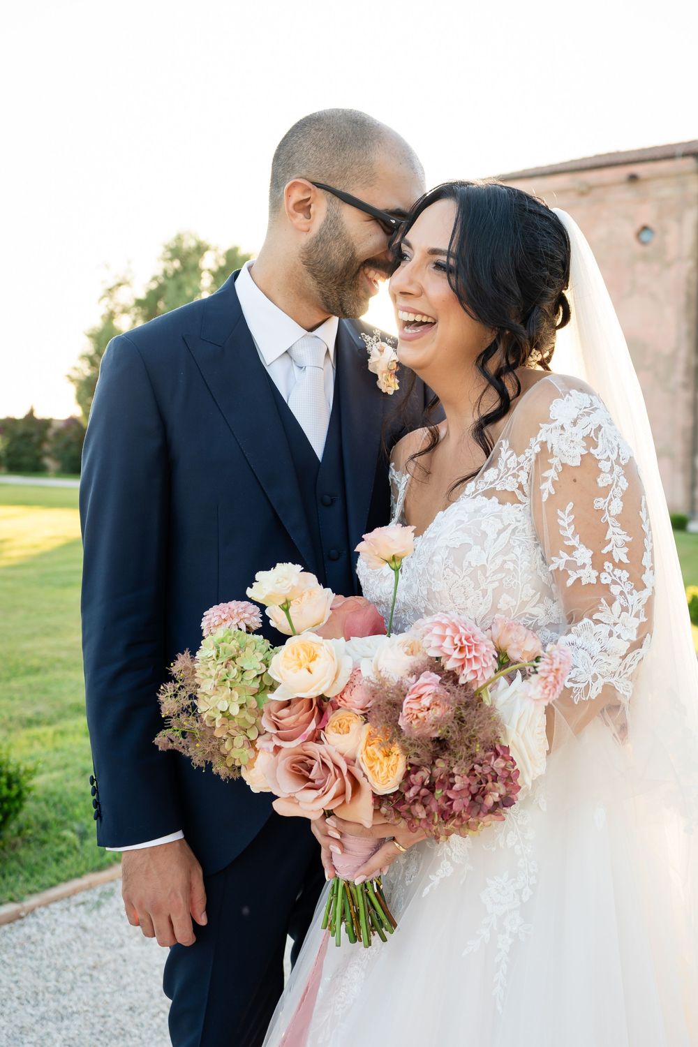A romantic wedding couple shares joyful moments together while holding a bouquet of pink and peach flowers.