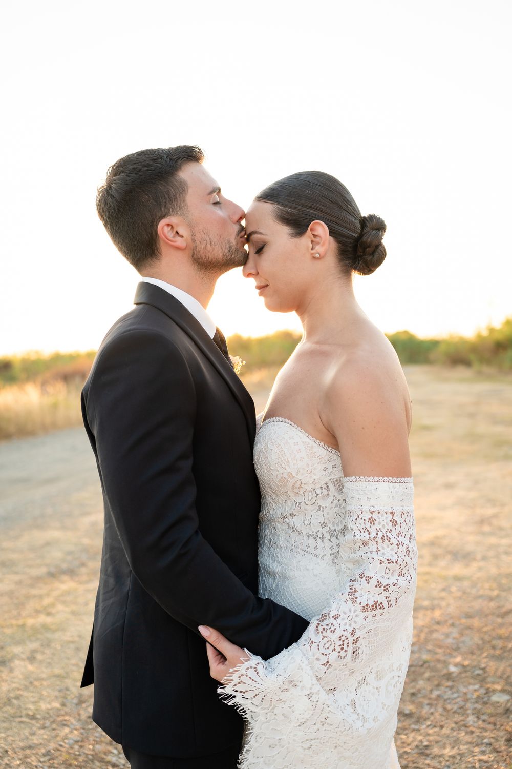 A romantic moment between newlyweds sharing laughter at sunset, with the bride in lace and groom in classic black suit.