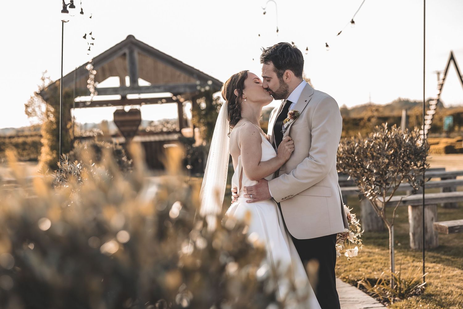 A natural photo of a newly married couple sharing a kiss in the wedding venue gardens.
