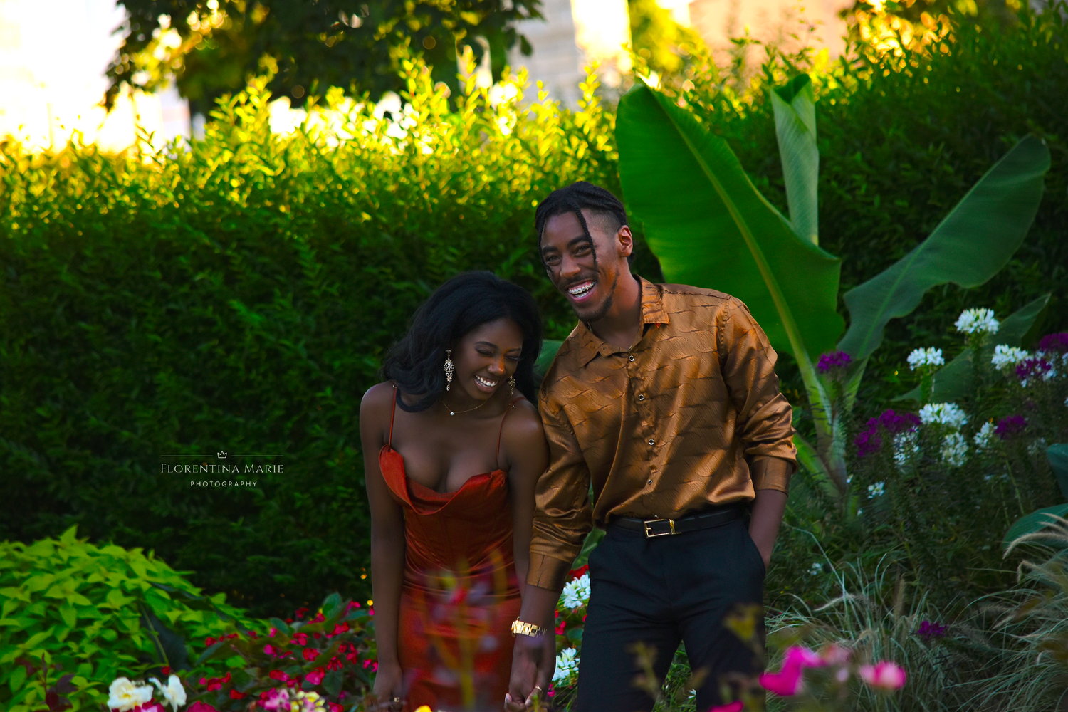 A couple embraces in a garden setting with vibrant purple flowers blooming in the background.