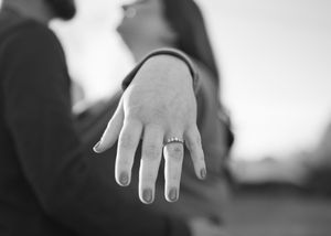 Close-up black and white photo of hand displaying engagement ring.