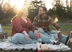 Couple enjoying romantic picnic on blanket with wine and snacks at sunset.