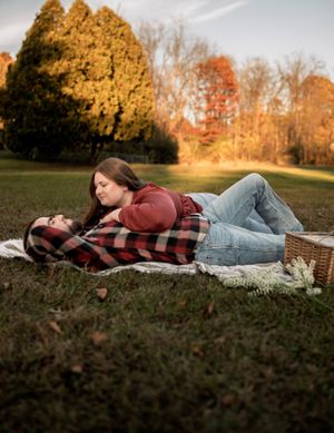 Couple lying on picnic blanket during autumn sunset with picnic basket nearby.