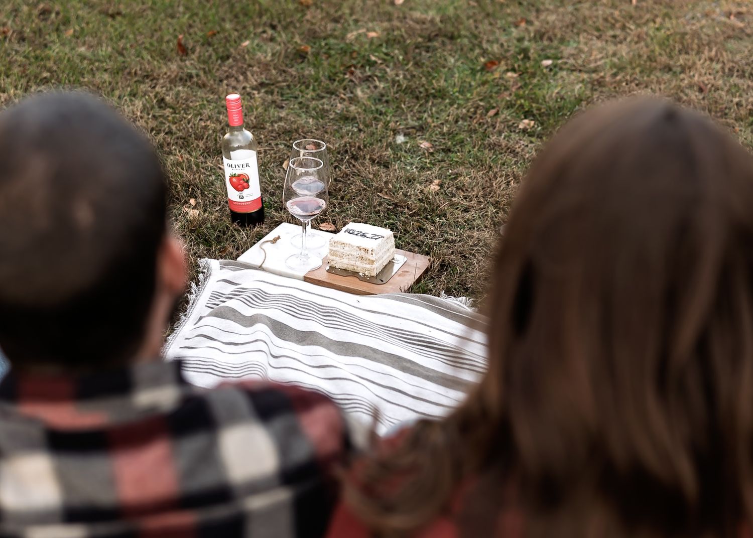 Overhead view of romantic picnic setup with wine and snacks on white blanket.